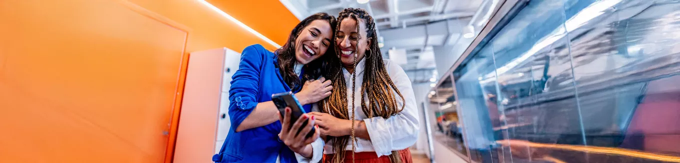 duas mulheres rindo enquanto olham algo em celular.