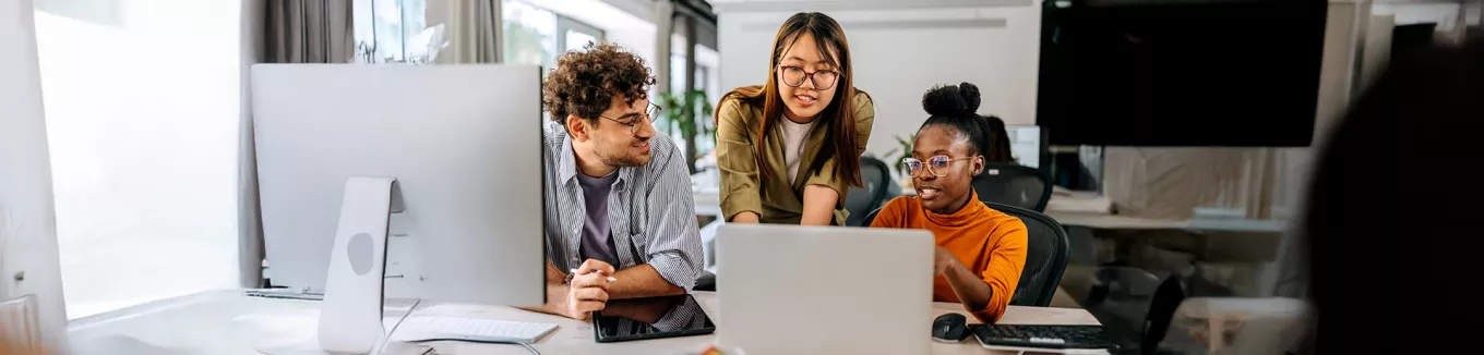 três pessoas conversando enquanto olham algo em computador.