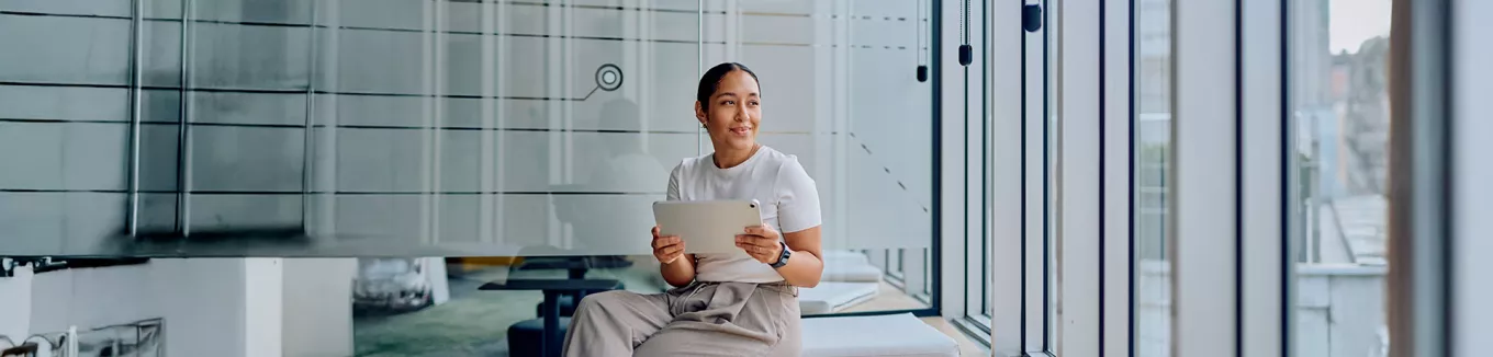 mulher segurando tablet e olhando pela janela em escritório.