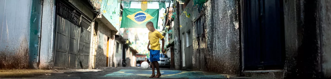 Foto mostra um menino jogando bola em uma rua enfeitada para a Copa do Mundo