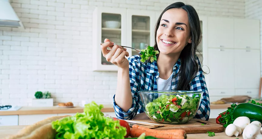 Foto mostra uma mulher comendo salada no seu almoço de home office