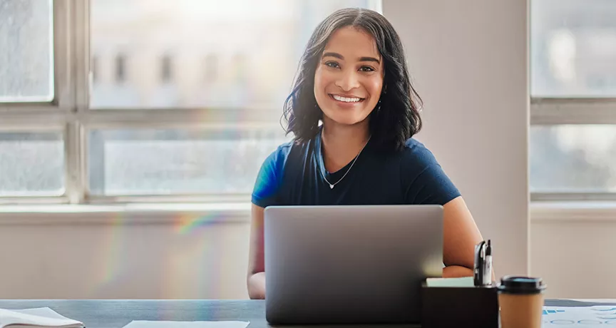 mulher sorrindo para a câmera enquanto usa notebook.